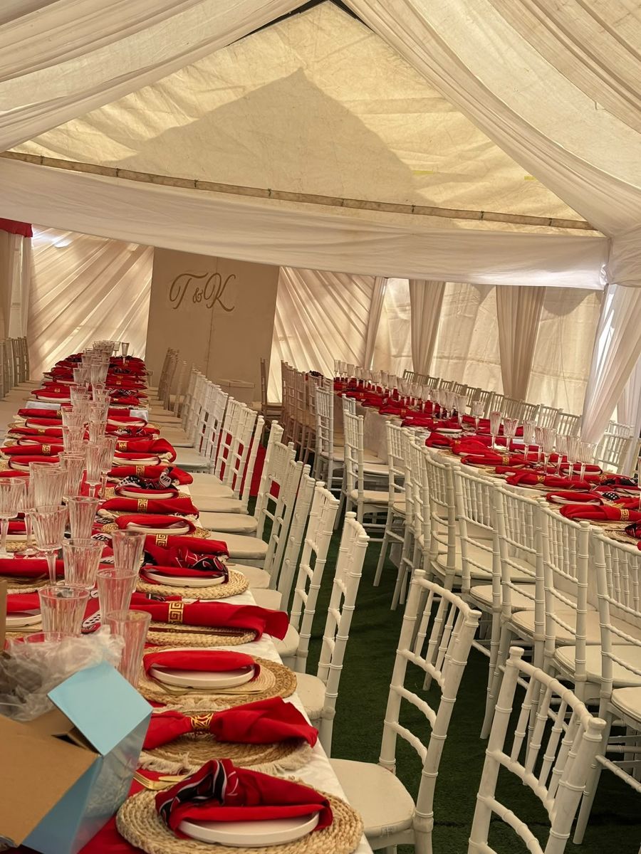 Long reception tables with red napkins and white chairs inside a white tent