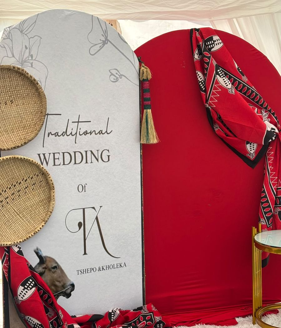 Traditional wedding welcome board with a red and black patterned backdrop and woven baskets